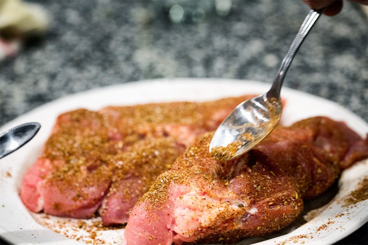 Sprinkling spice rub on pork